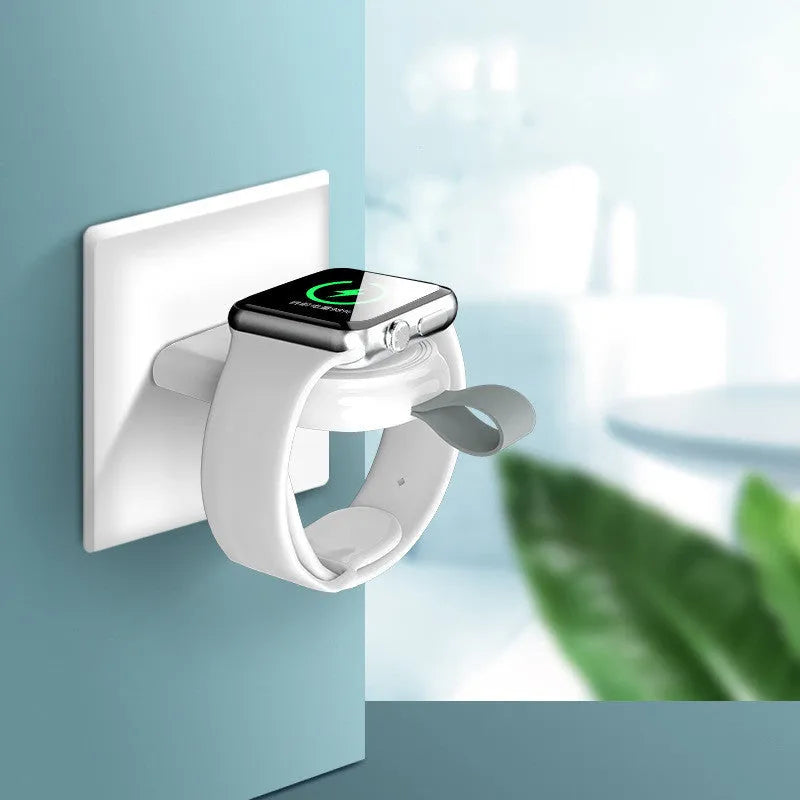 Portable white wireless charging dock for Apple Watch on a desk next to a laptop.