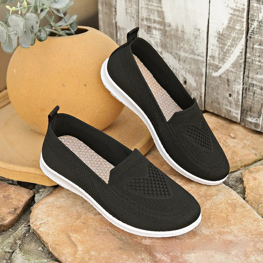Women's beige canvas slip-on shoe with heart-shaped perforations and a flat sole.