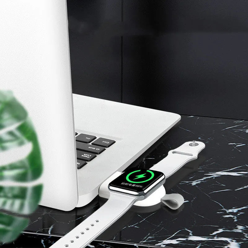 Portable white wireless charging dock for Apple Watch on a desk next to a laptop.