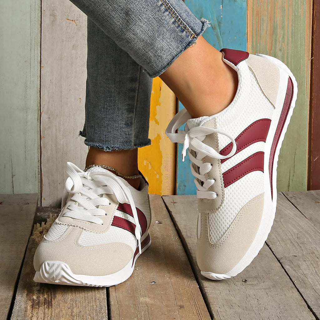 Wine red women's low-top sneaker with mesh upper, synthetic leather accents, and elastic cross straps on a flat rubber sole.