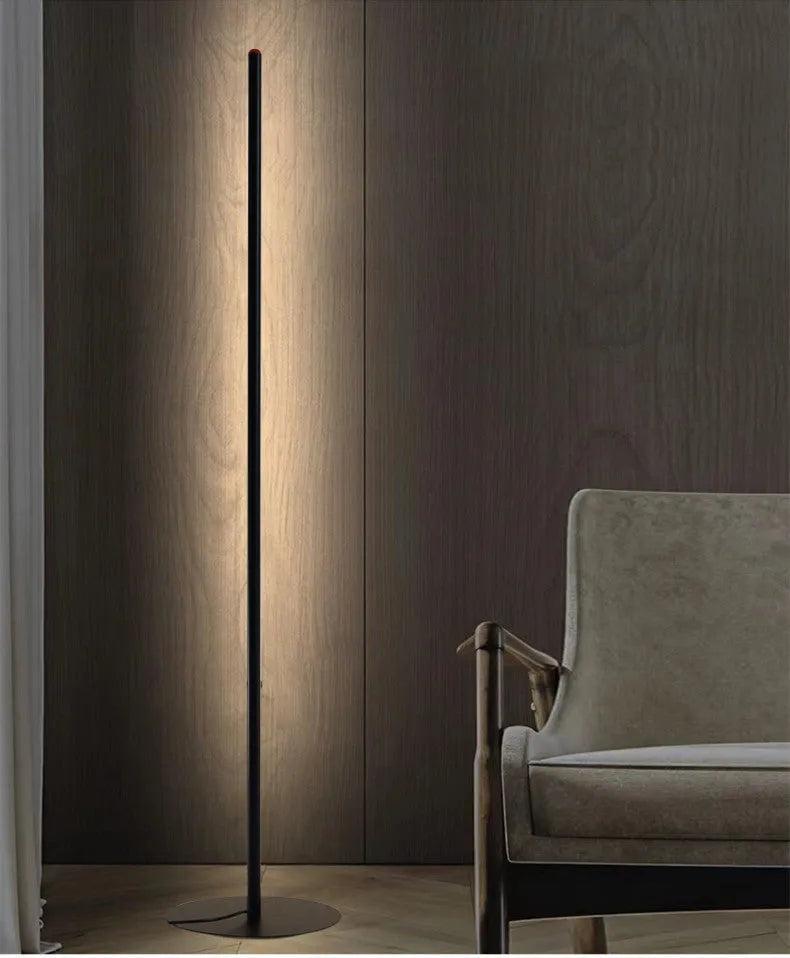 Modern vertical aluminium alloy floor lamp in silver, shown beside a sofa in a living room setting.