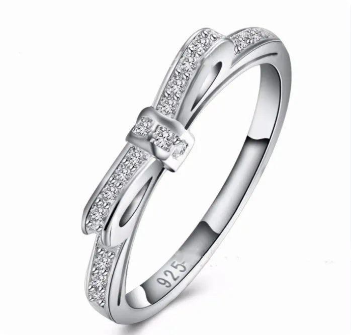 Silver coloured bow-shaped ring with rhinestone and zircon crystal decoration on a model's finger.