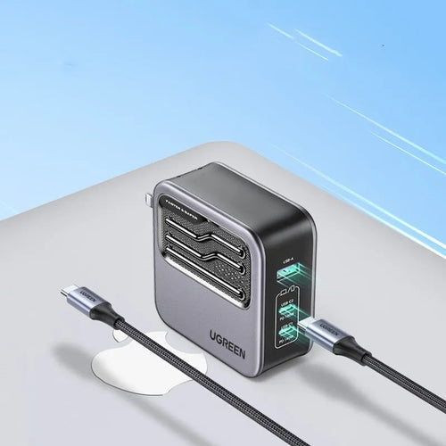 100W Gallium Nitride fast wall charger with USB-C port on a desk next to a laptop.