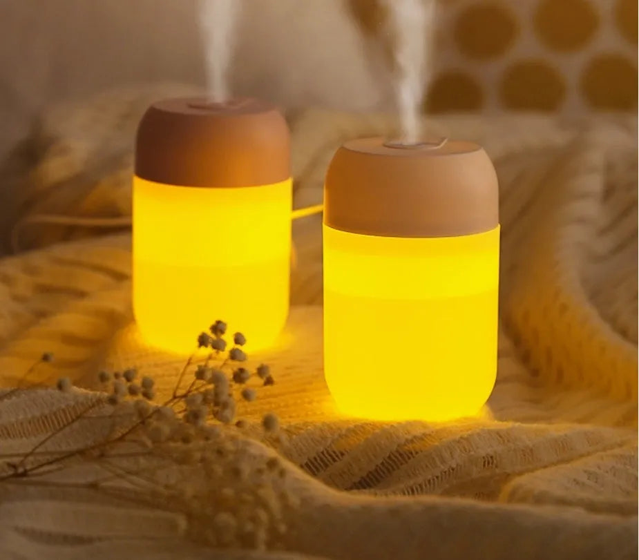 Small white cylindrical USB-powered humidifier with charging cable on a desk.