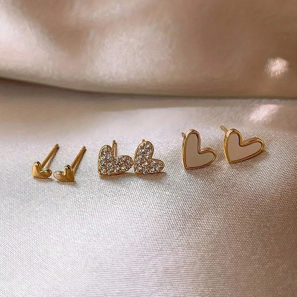 Three pairs of heart-shaped alloy earrings with love motif in gold, black, black and white, and pink colours.