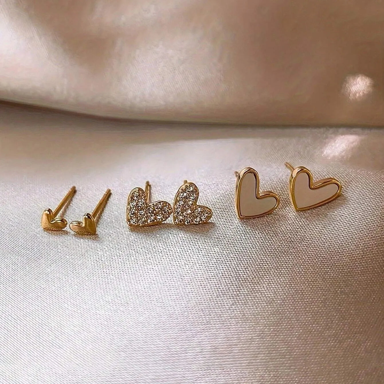 Three pairs of heart-shaped alloy earrings with love motif in gold, black, black and white, and pink colours.