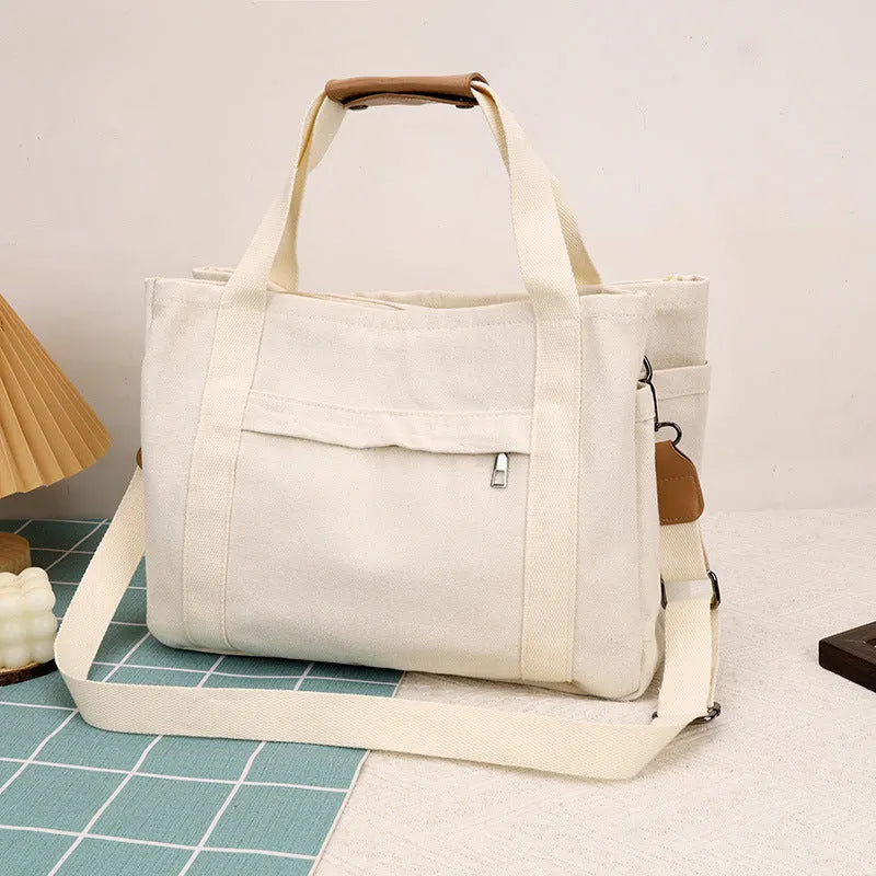 Khaki canvas tote bag with zipper closure showing internal camera pocket and document bag compartments.