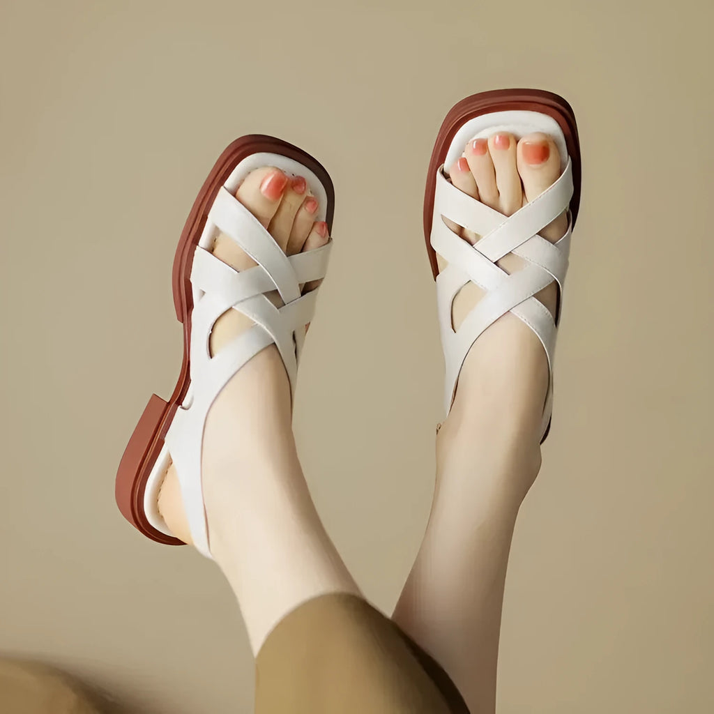 Women's glossy black patent leather sandals with square toe and cross-belt fastening on a light background.