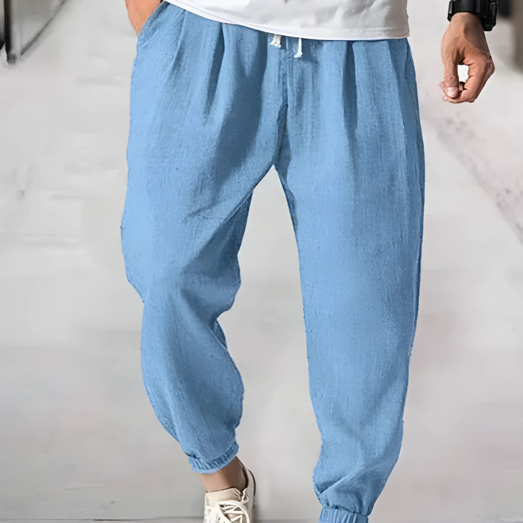 Men's loose fit cotton trousers with elasticated ankle bands in light green, shown in a casual summer setting.
