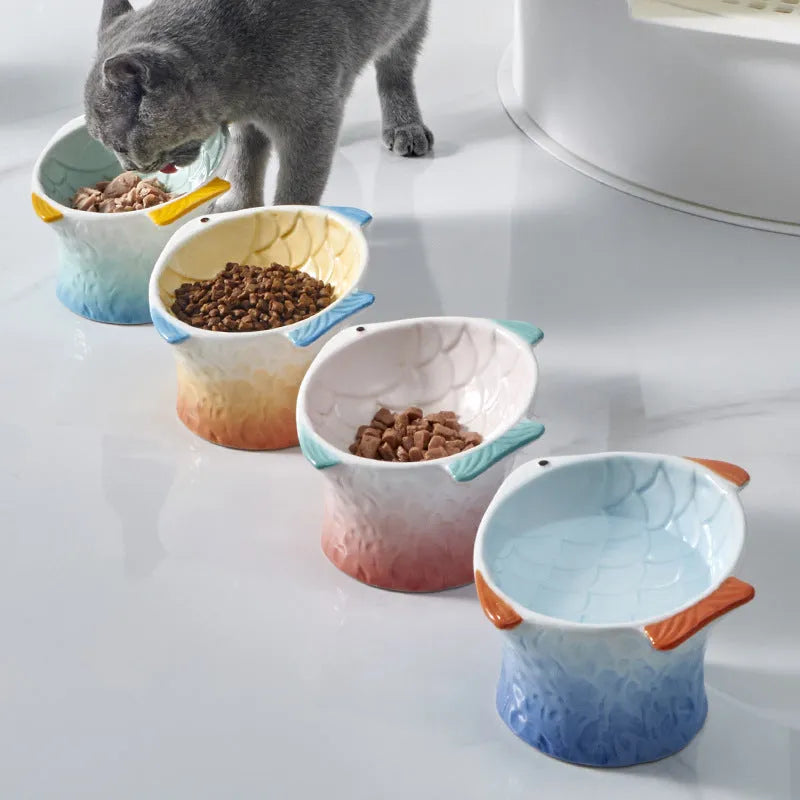 Set of four coloured fish-shaped ceramic cat bowls with elevated tilt design on a table.