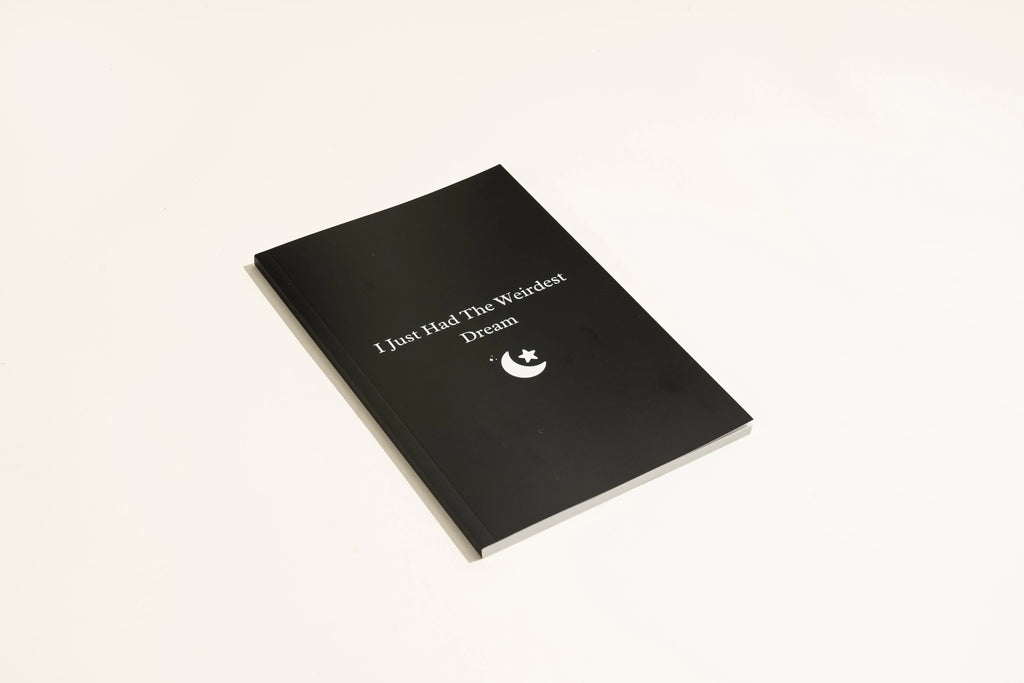 Black soft-touch dream journal notebook lying open on a table, showing ruled pages.