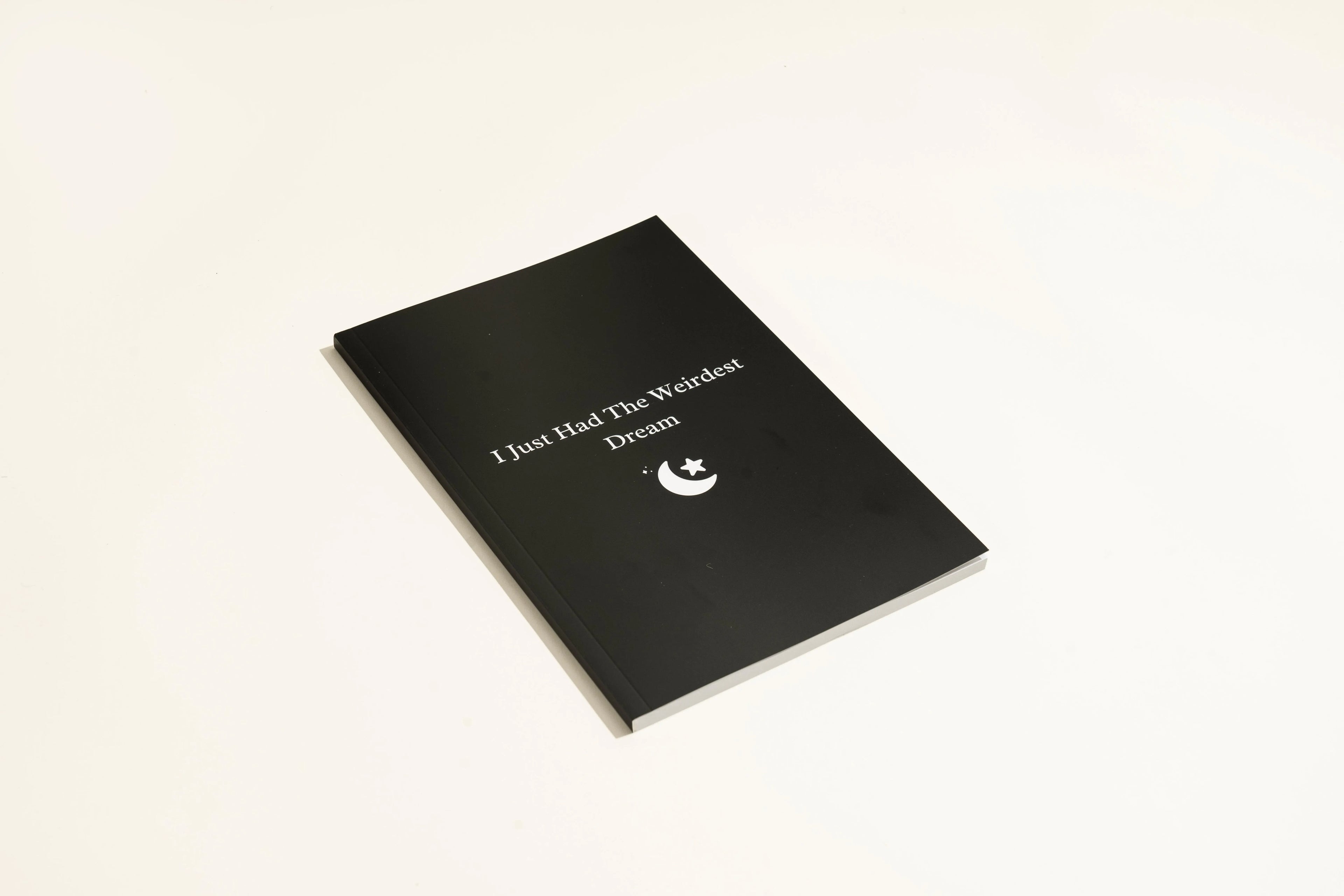 Black soft-touch dream journal notebook lying open on a table, showing ruled pages.