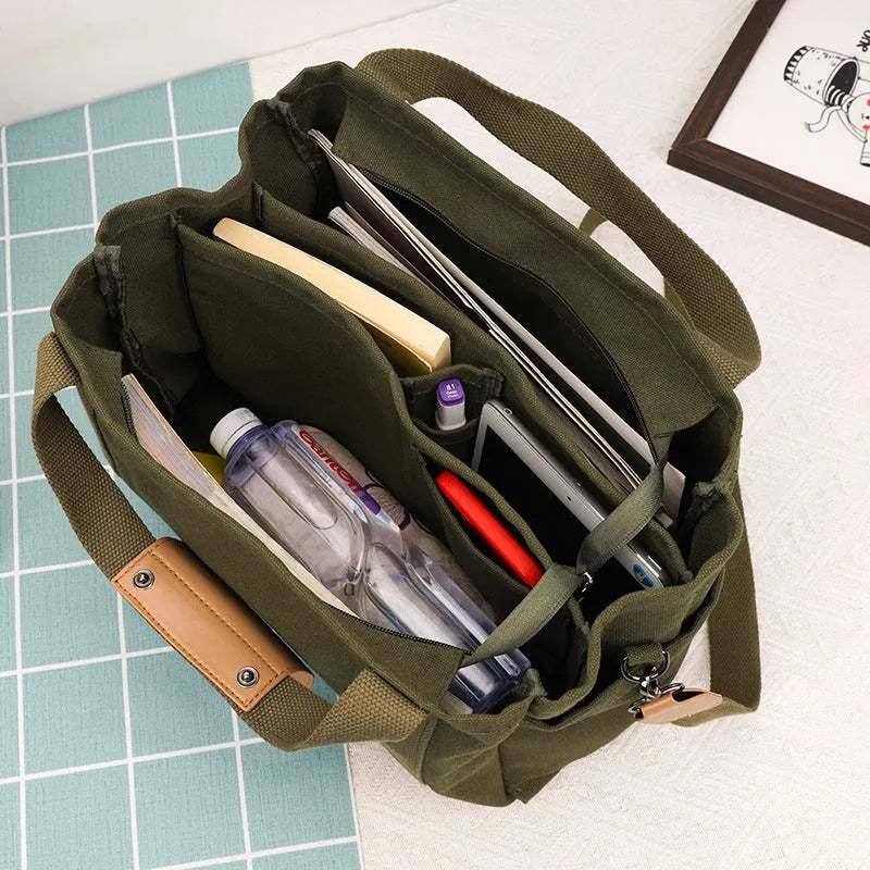 Khaki canvas tote bag with zipper closure showing internal camera pocket and document bag compartments.