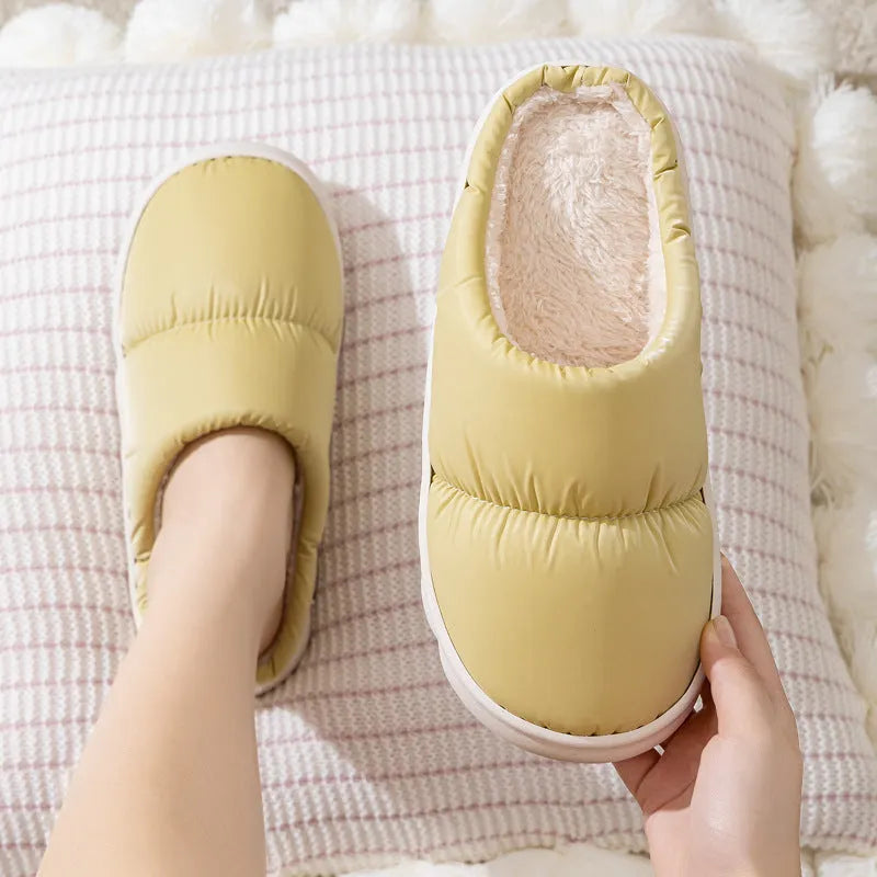A pair of thick-soled house slippers with an artificial leather upper and plush lining, shown in a choice of colours.