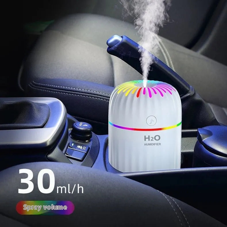 A green USB mini car aromatherapy humidifier on a desk next to a laptop, showing its compact size.