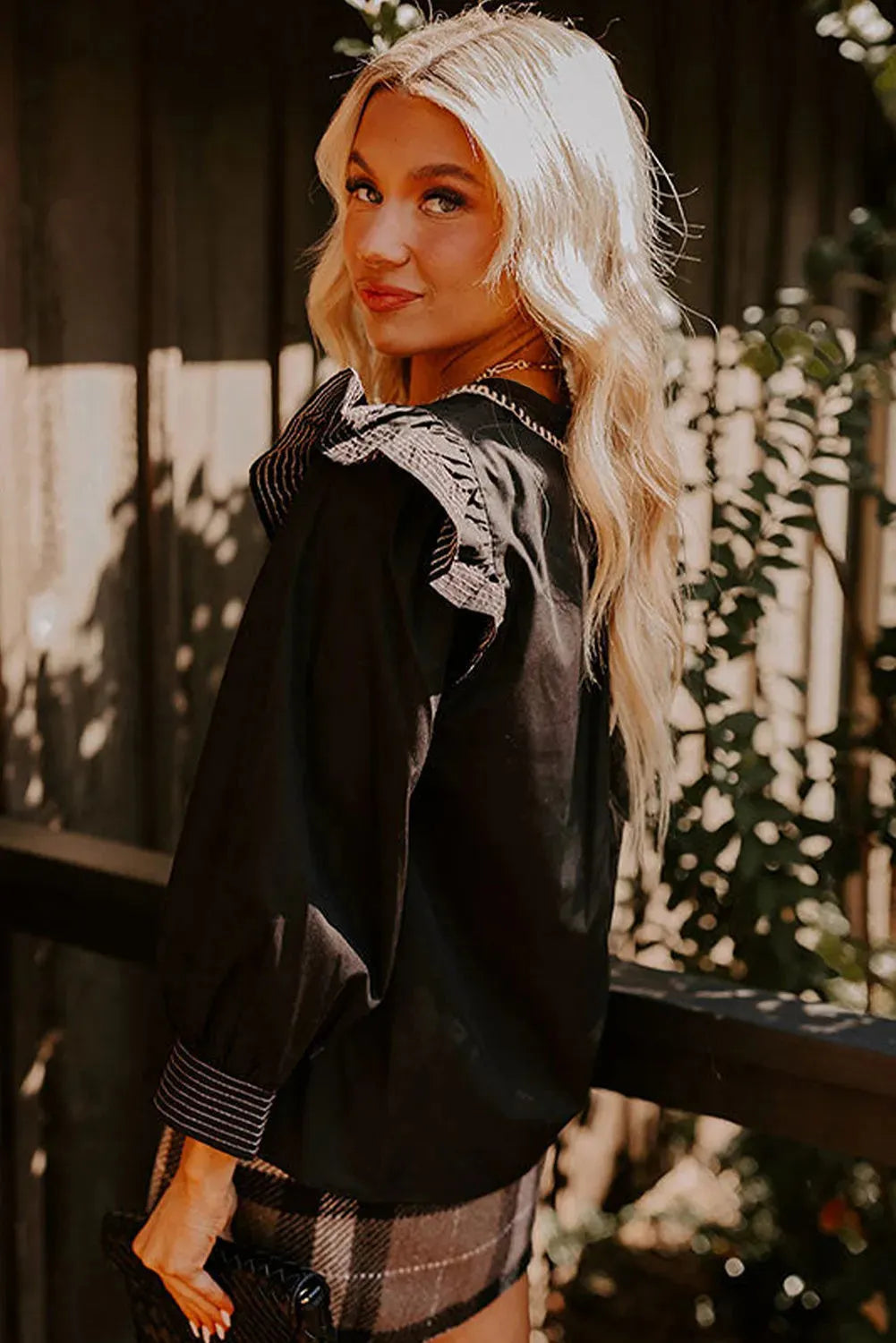 Black women's V-neck blouse with contrast stitching on the neckline and long sleeves with a ruffle detail.