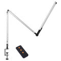 Aluminium clip-on desk lamp with adjustable arm and remote control on a wooden desk.