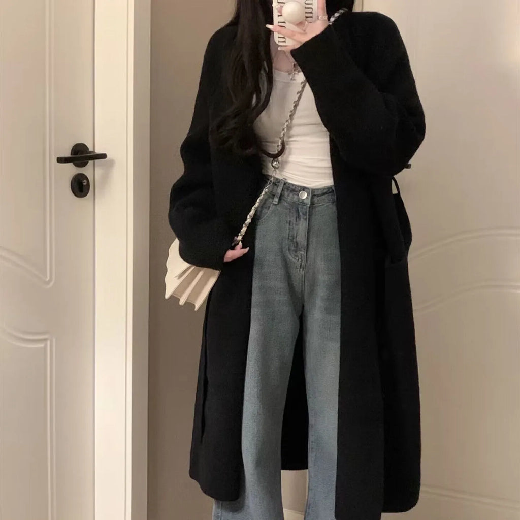 Woman wearing a loose, thick dark gray knitted cardigan with a 3D pattern and long sleeves.