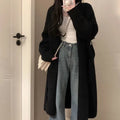 Woman wearing a loose, thick dark gray knitted cardigan with a 3D pattern and long sleeves.