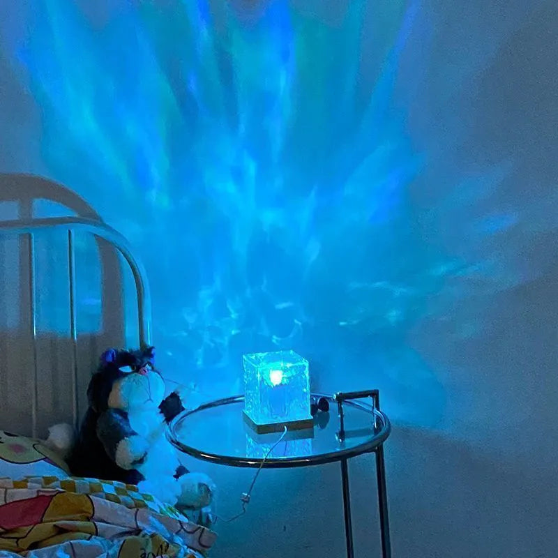 Modern geometric crystal table lamp projecting colourful water ripple light effect on wall.