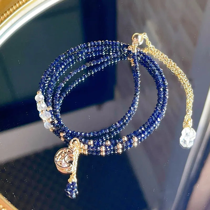 Close-up of a women's multi-layer bracelet with three blue gold sand stone rings on a wrist.