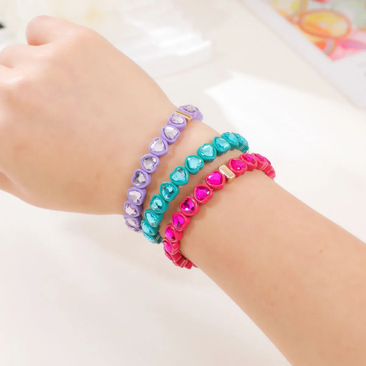 Colourful enamel heart-shaped charm on a stretch bracelet with diamond-textured alloy finish.