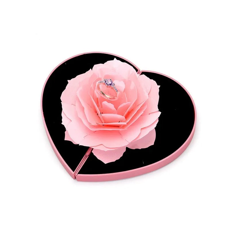 Red heart-shaped plastic ring box on a white background, showing its rotating mechanism.
