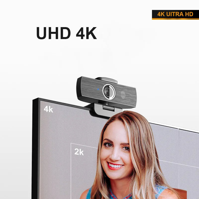 Black USB computer webcam with a magnetic privacy cover on a desk next to a laptop