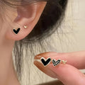 Three pairs of heart-shaped alloy earrings with love motif in gold, black, black and white, and pink colours.