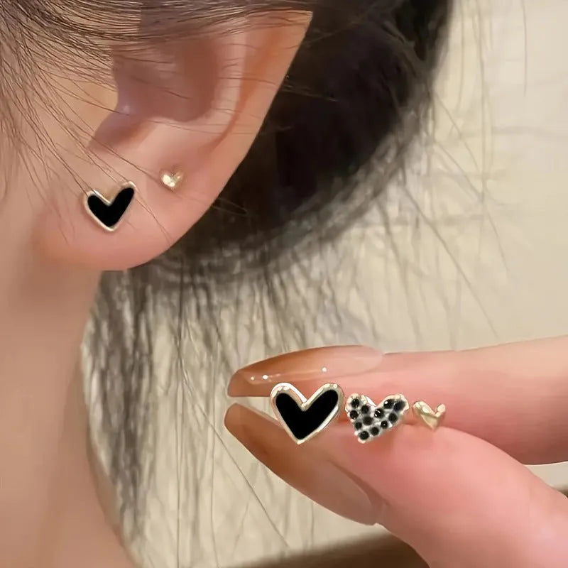 Three pairs of heart-shaped alloy earrings with love motif in gold, black, black and white, and pink colours.