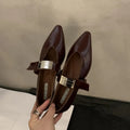 Women's black pointed toe Mary Jane shoes with a silver buckle on a low flat heel.