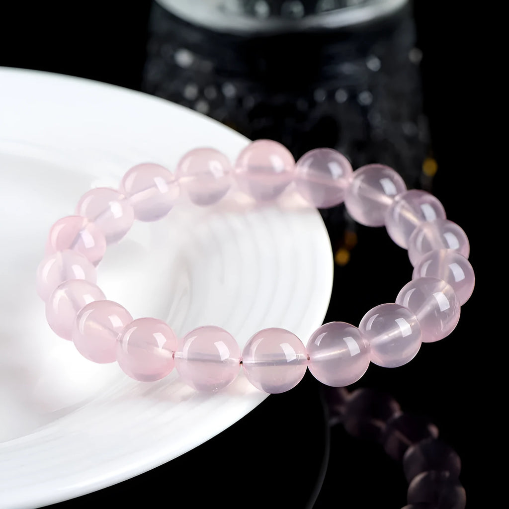 A pink natural crystal bead bracelet with polished round beads in a single circle design on a wrist.