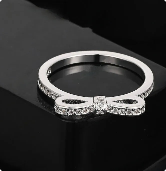 Silver coloured bow-shaped ring with rhinestone and zircon crystal decoration on a model's finger.