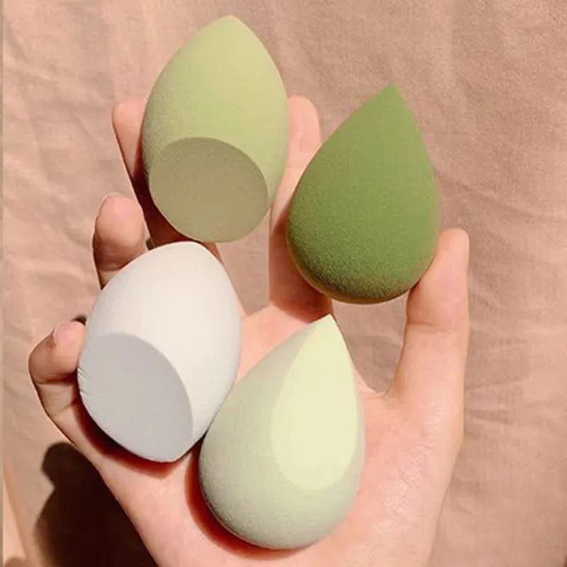 Set of seven differently shaped coloured makeup sponges including pear, heart, and drop shapes on a white background.