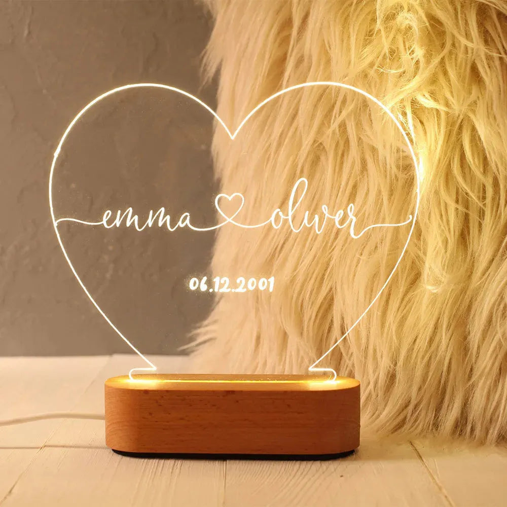Custom transparent acrylic LED night light engraved with personal names and a date on a bedside table.