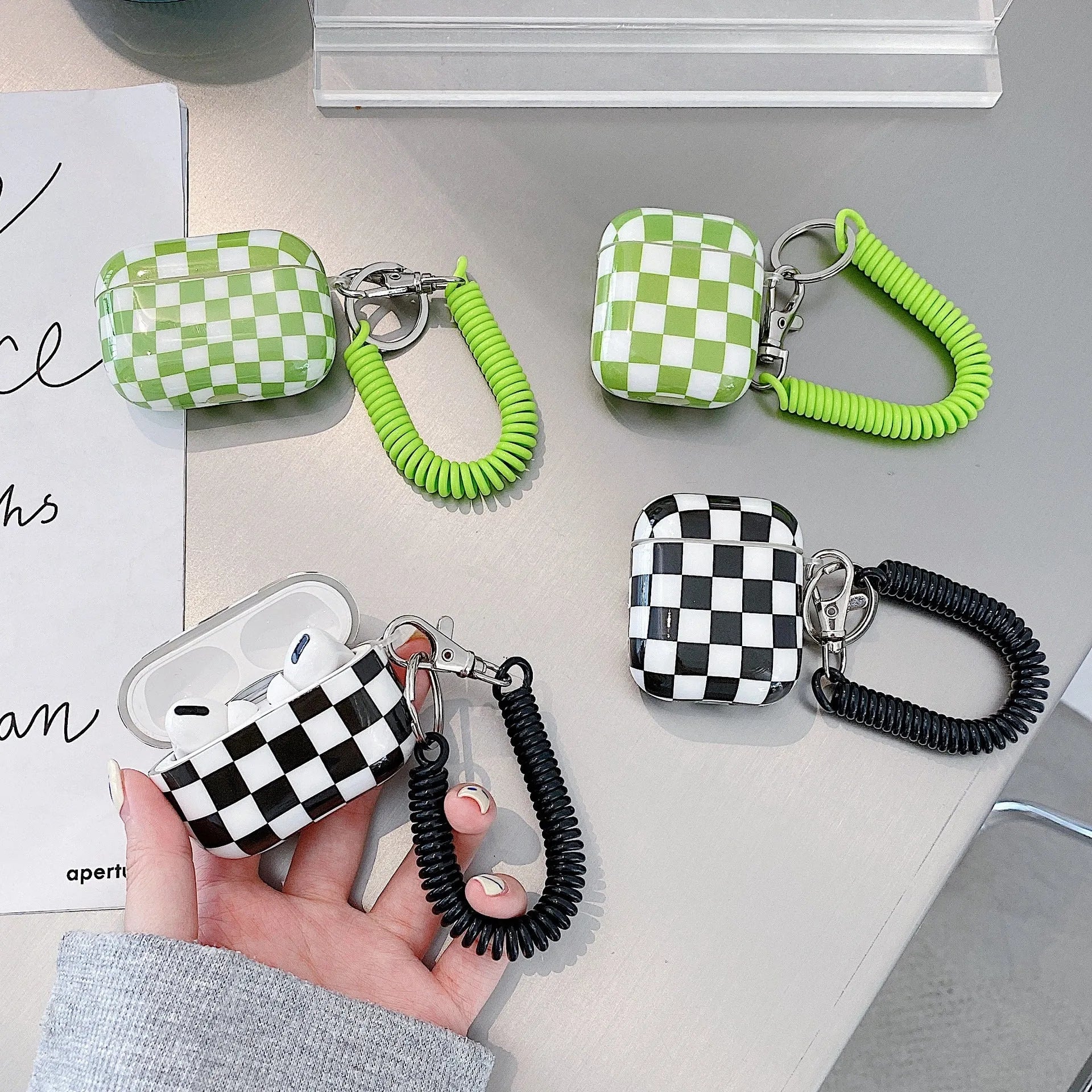 Black and green checkerboard pattern TPU protective case covers for Apple AirPods, one with a smiley face lanyard.