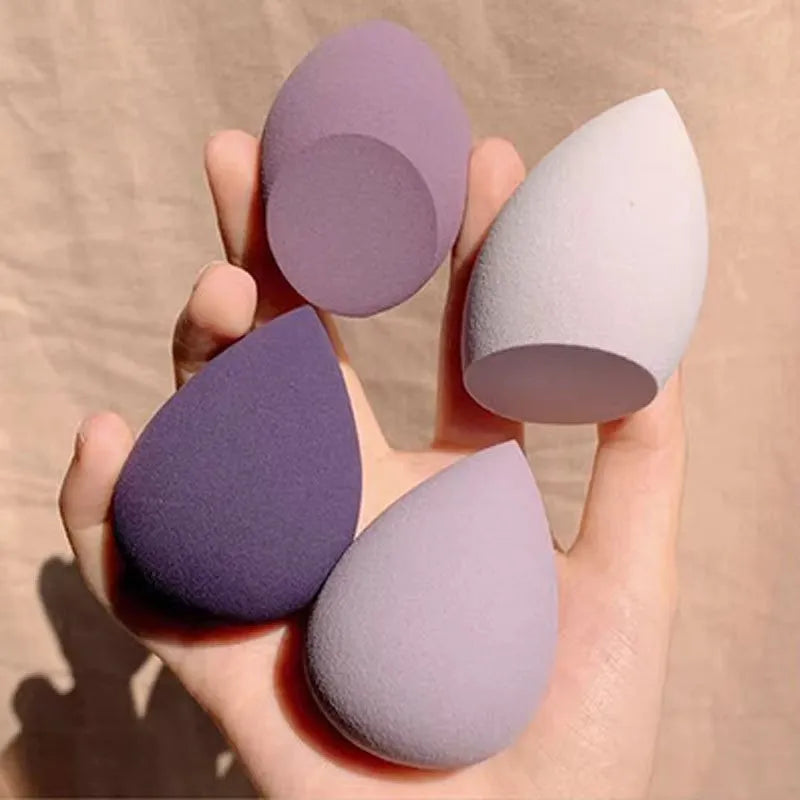 Set of seven differently shaped coloured makeup sponges including pear, heart, and drop shapes on a white background.