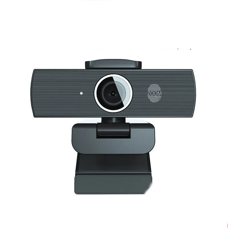 Black USB computer webcam with a magnetic privacy cover on a desk next to a laptop