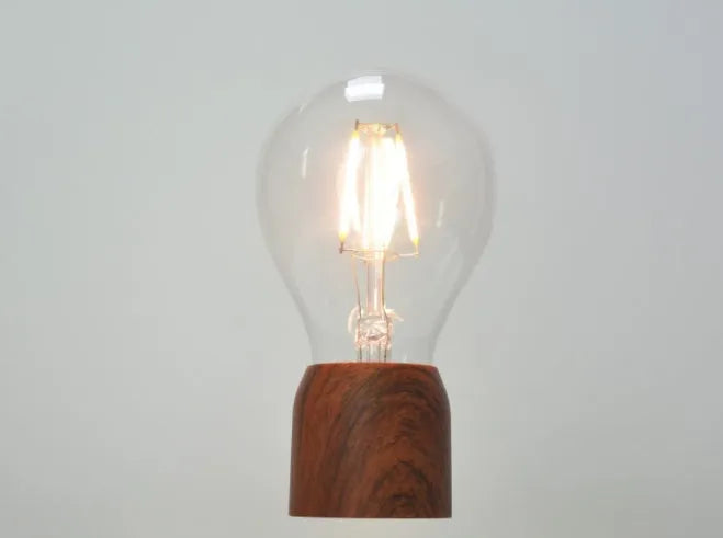 Magnetic levitation light bulb floating above wood-effect base with international plug adapters