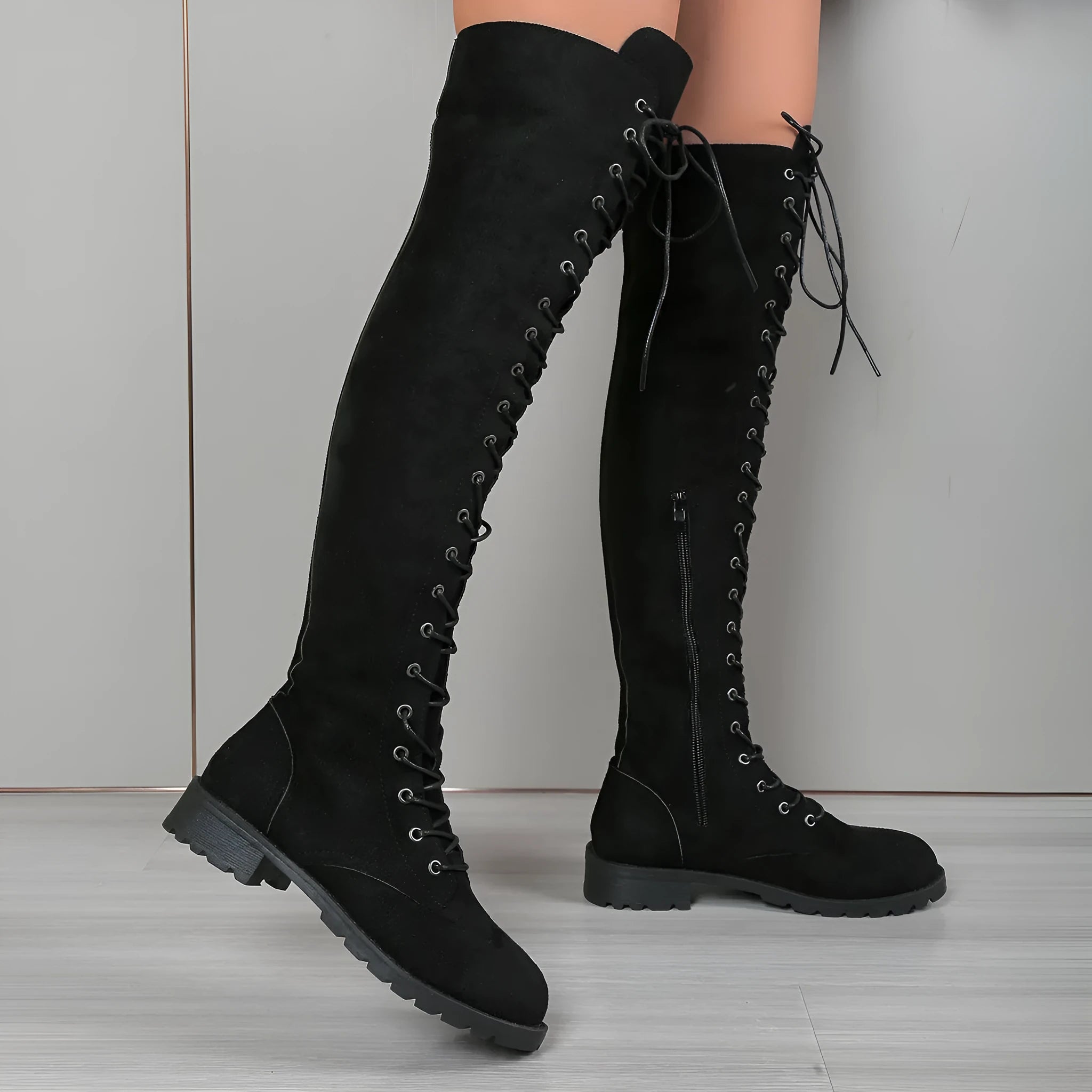 Black lace-up over the knee boots with a round toe and flat rubber sole on a plain background.