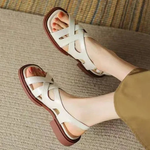 Women's glossy black patent leather sandals with square toe and cross-belt fastening on a light background.
