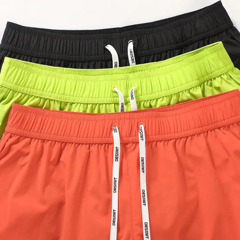 Man wearing loose orange polyester shorts on a beach, showcasing the elastic waist and fit for surfing.