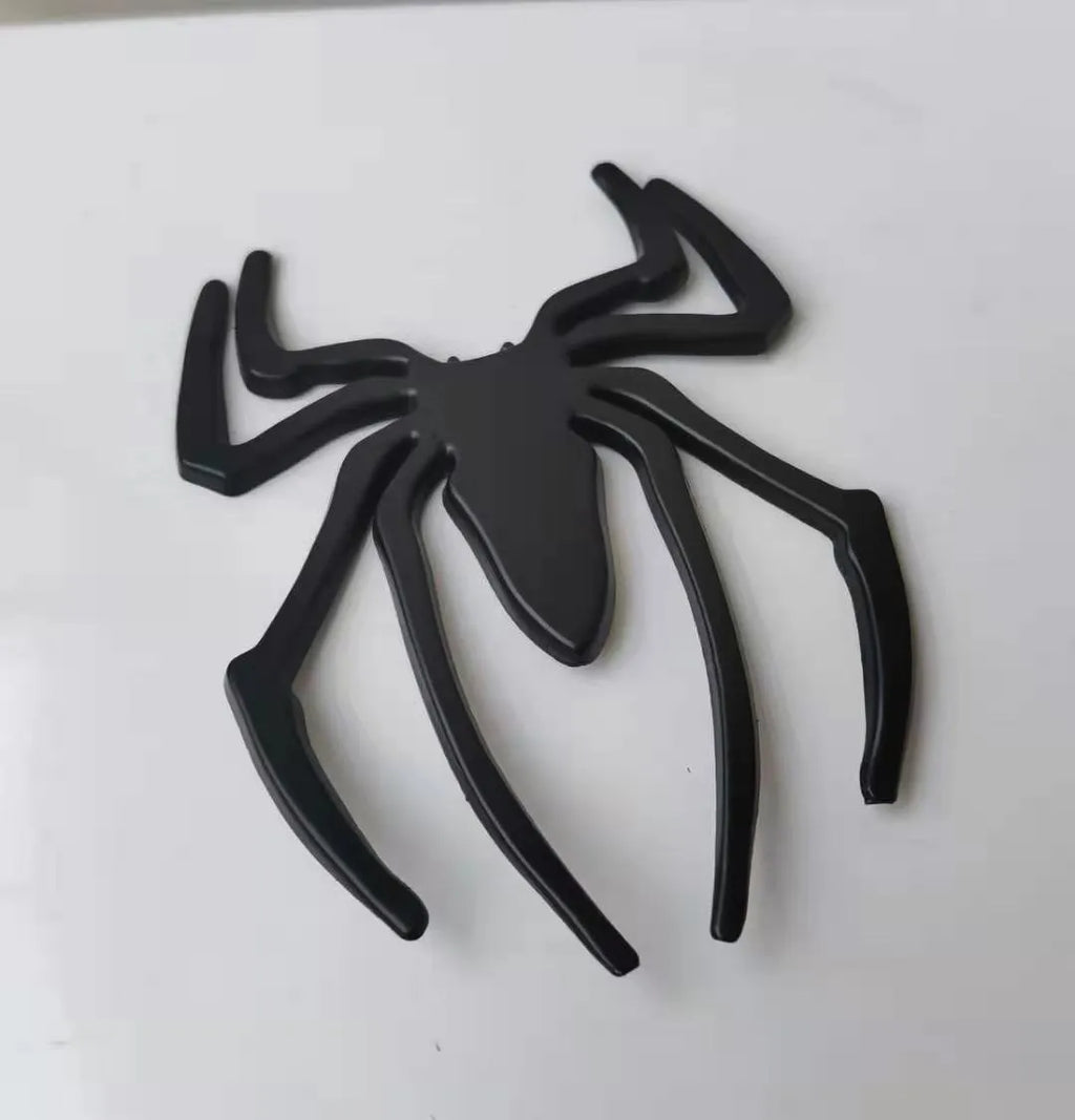 Three-dimensional metal spider bumper sticker in zinc alloy, shown in gold colour, measuring 7 by 5 cm.