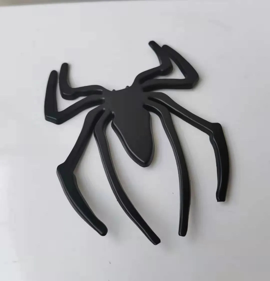 Three-dimensional metal spider bumper sticker in zinc alloy, shown in gold colour, measuring 7 by 5 cm.