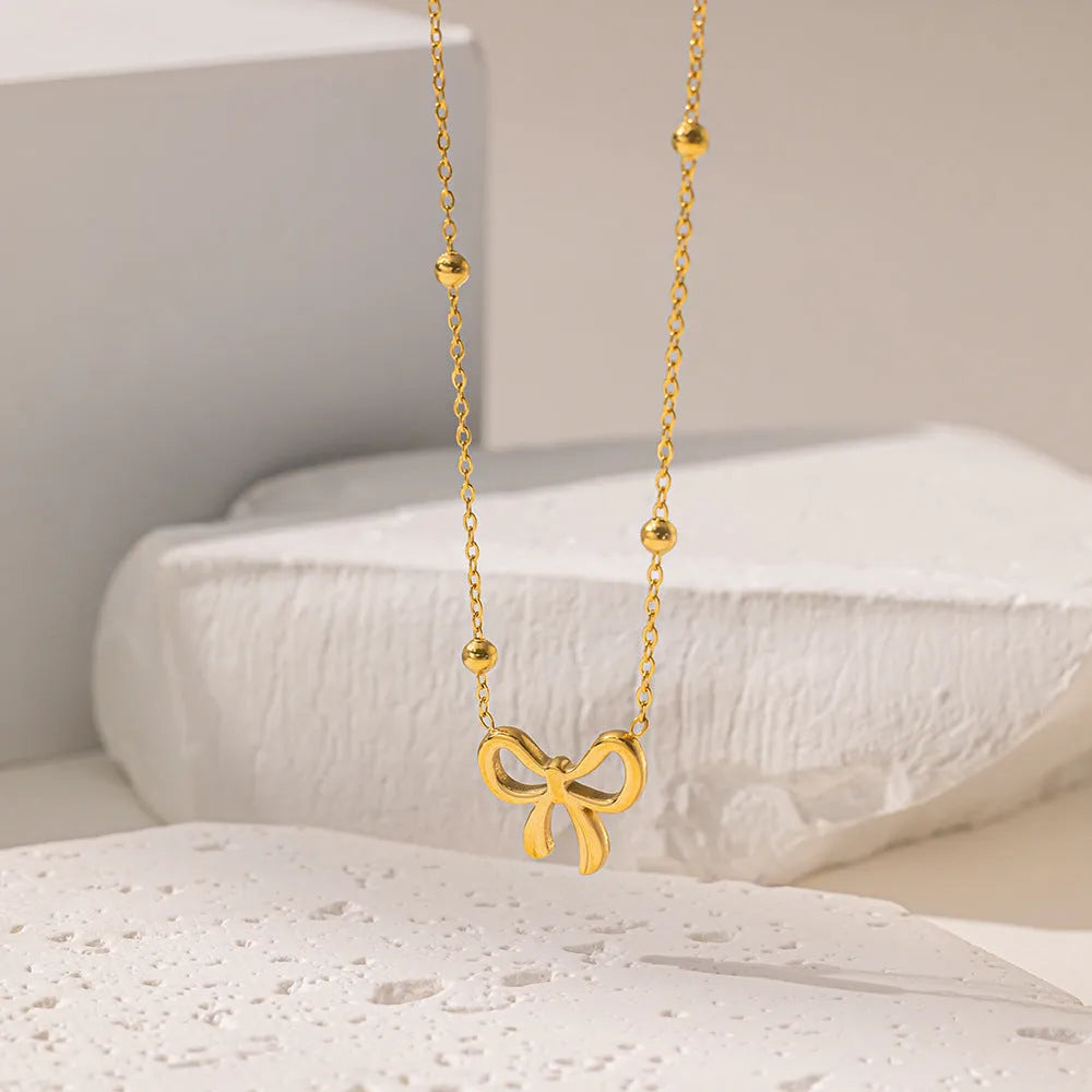 Gold coloured bow pendant necklace on a cross chain, showing adjustable length.