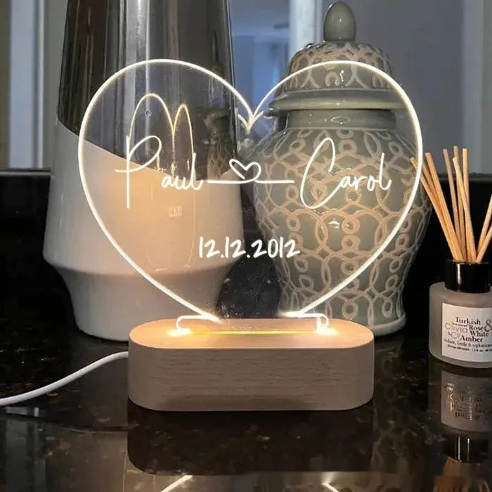 Custom transparent acrylic LED night light engraved with personal names and a date on a bedside table.