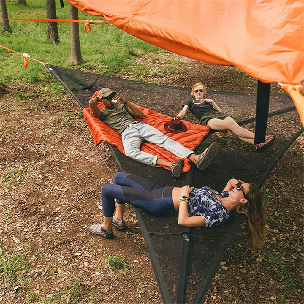 Black polyester portable multi-person triangle hammock lying on grass with trees in background