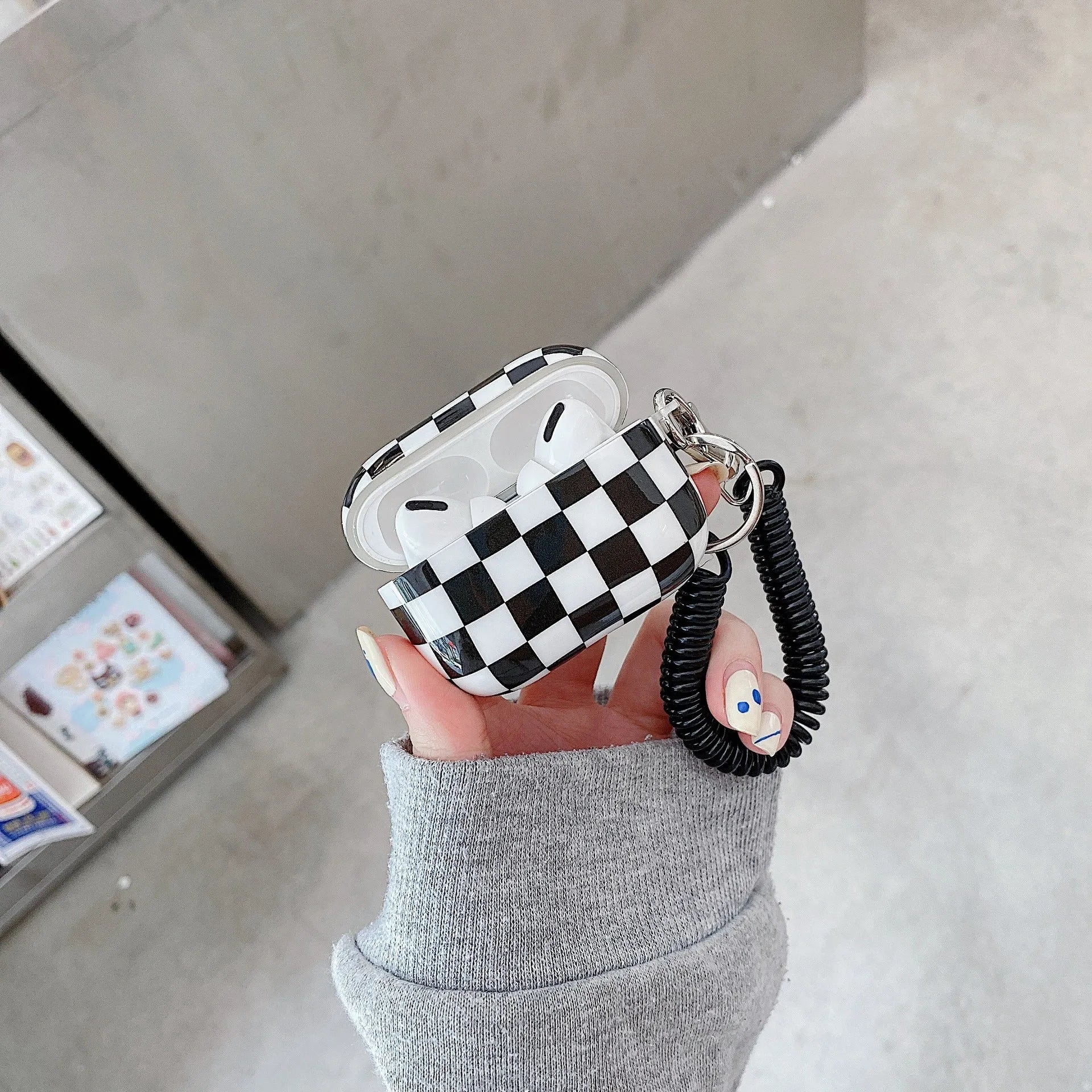 Black and green checkerboard pattern TPU protective case covers for Apple AirPods, one with a smiley face lanyard.