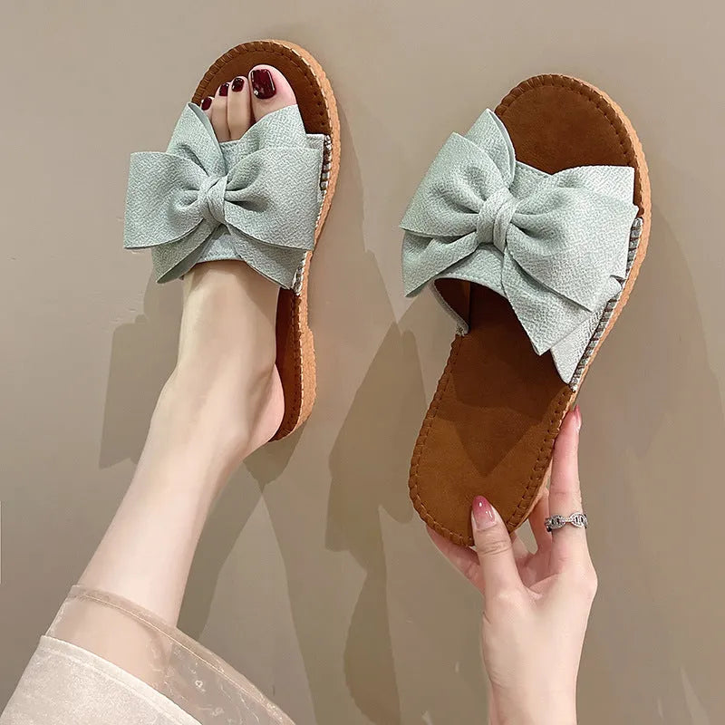 Women's beige suede slip-on sandals with bow detail and flat rubber sole