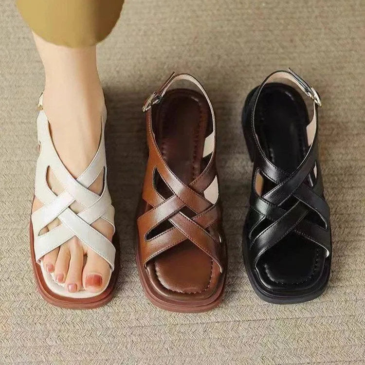 Women's glossy black patent leather sandals with square toe and cross-belt fastening on a light background.